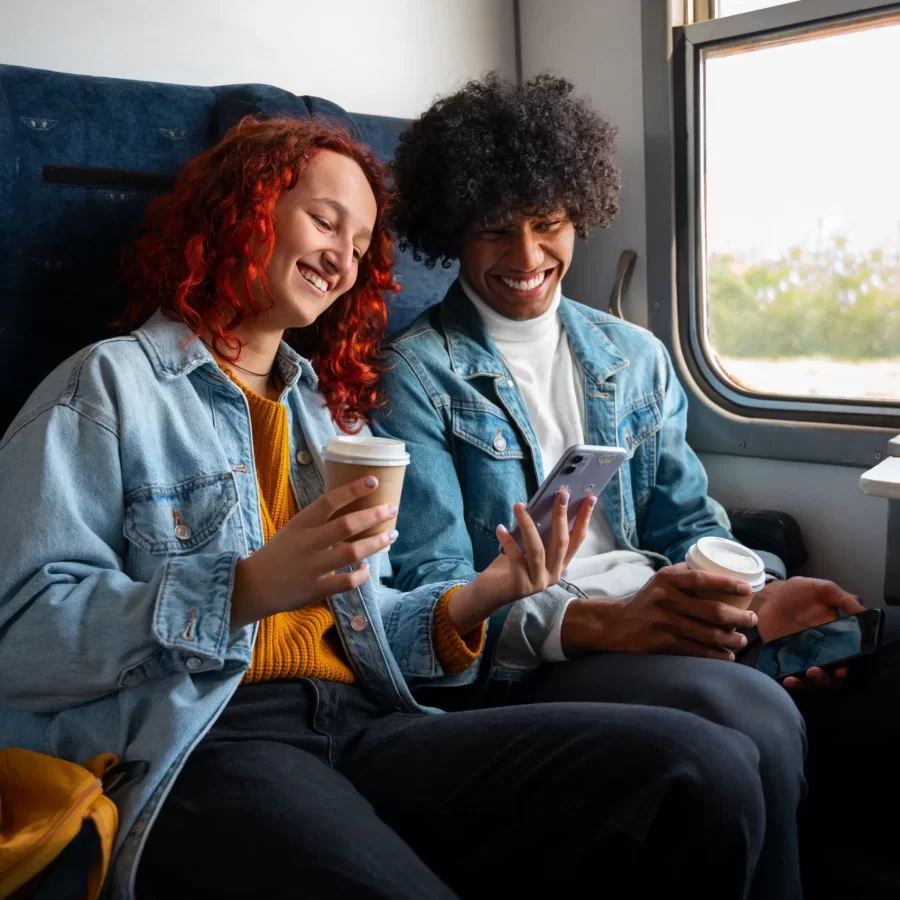 Une femme et un homme assis l'un à côté de l'autre dans un train et regardant quelque chose sur son téléphone.